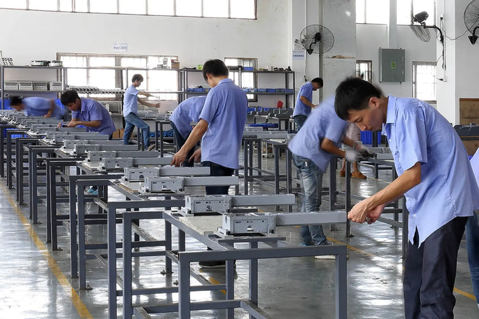 Workers in a factory setting with machinery and tables.