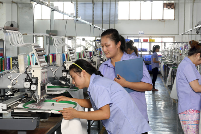 Workers in a factory setting with sewing machines and materials.