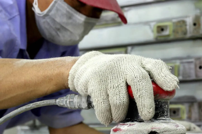 Person wearing gloves and a mask using a power tool in an industrial setting