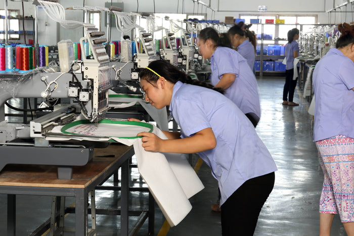 Factory workers operating sewing machines in a busy production line.
