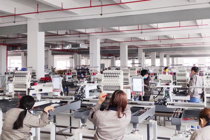 Factory interior with workers operating embroidery machines.