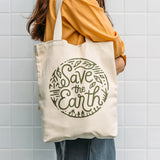 Person holding a tote bag with 'Save the Earth' text against a tiled wall.